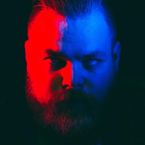 Musician Com Truise lit with saturated red light on the left side and strong blue light on the right.
