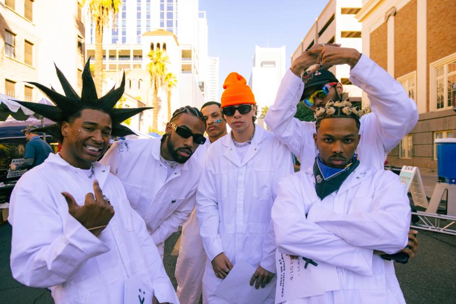Group of five attendees in white jumpsuits pose together outdoors.