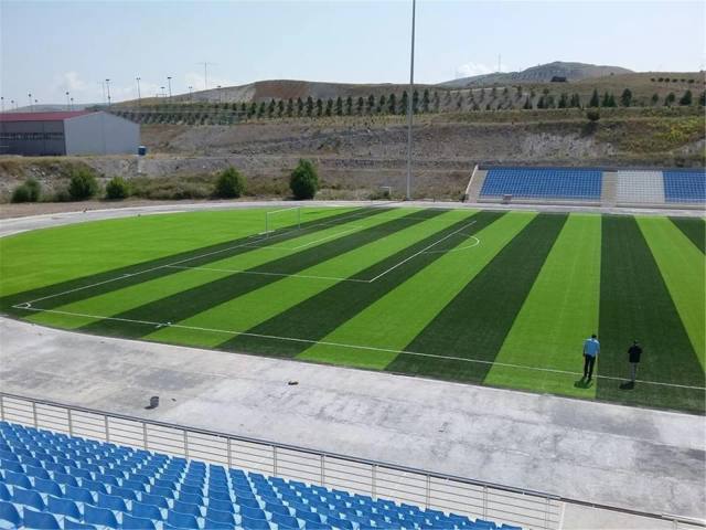 Mavi tribünlü stadyumda çizgili serilmiş suni çim saha