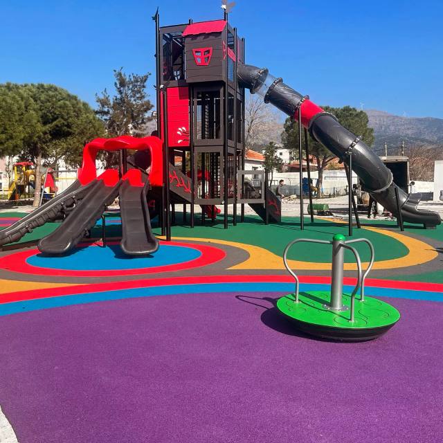 Gri ve kırmızı oyun kulesi ile mor, mavi ve kırmızı dökme kauçuk zemin uygulanmış park