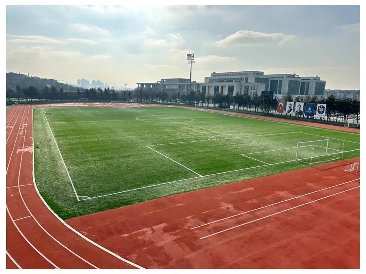 Tartan koşu pisti ile çevrelenmiş suni çim futbol sahası
