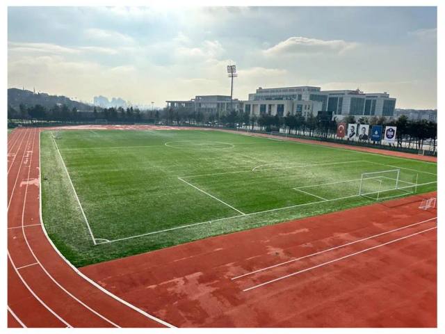 Tartan koşu pisti ile çevrelenmiş suni çim futbol sahası