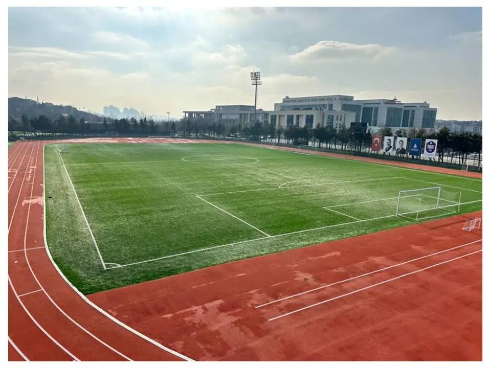 Tartan koşu pisti ile çevrelenmiş suni çim futbol sahası
