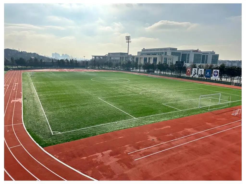 Tartan koşu pisti ile çevrelenmiş suni çim futbol sahası