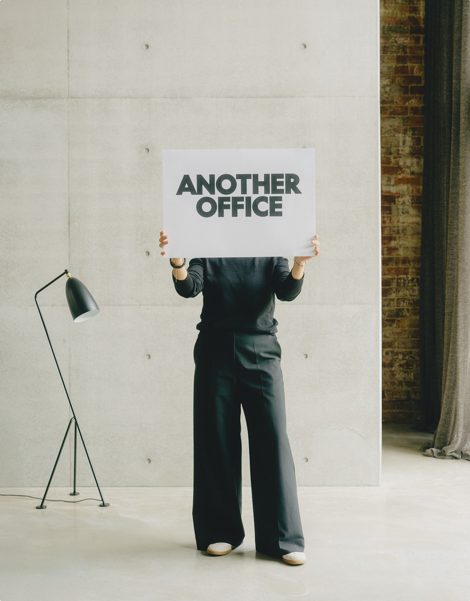 Person holding Another Office sign in a studio interior.