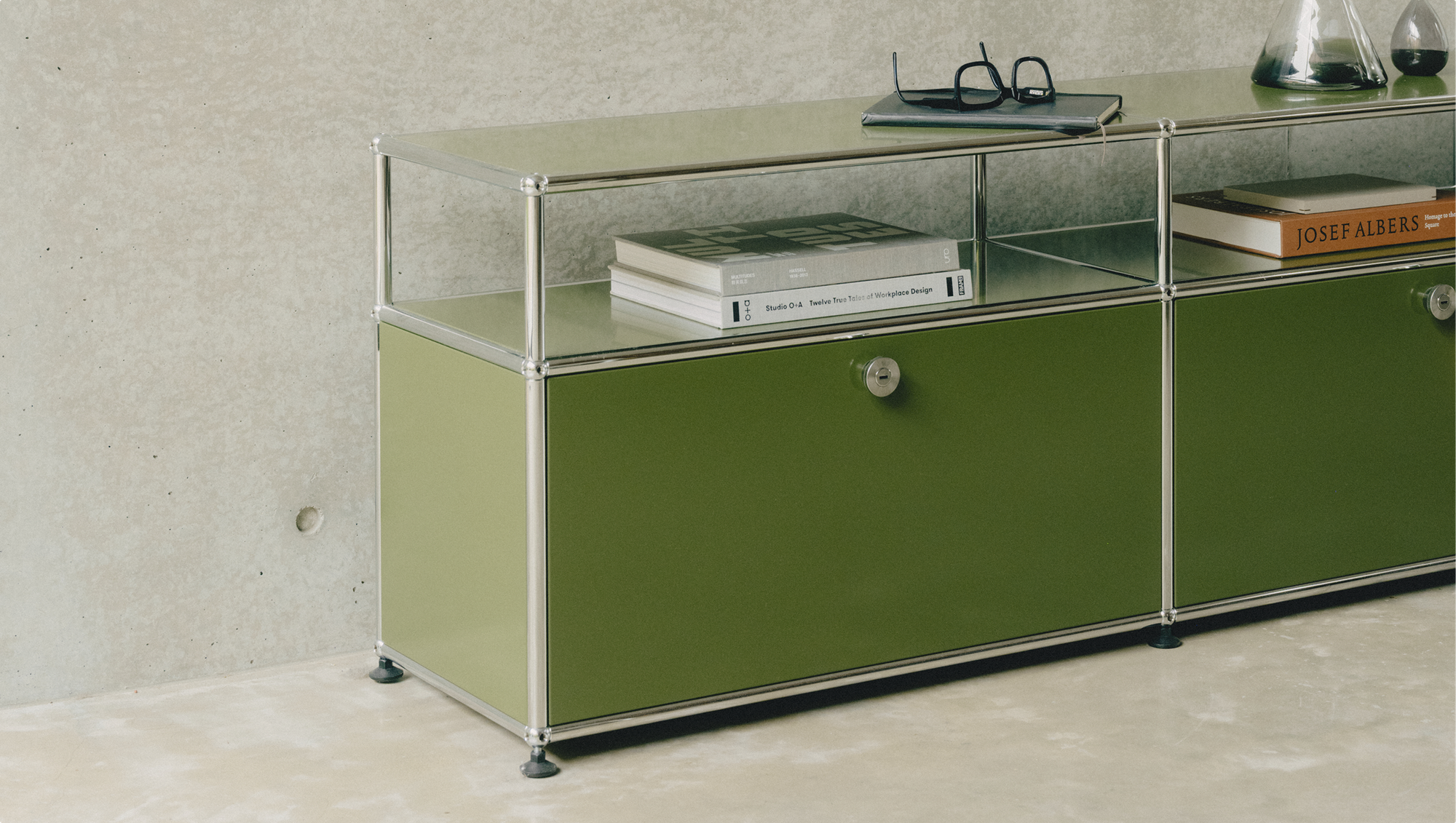 USM Haller storage unit with olive green doors against a concrete wall.