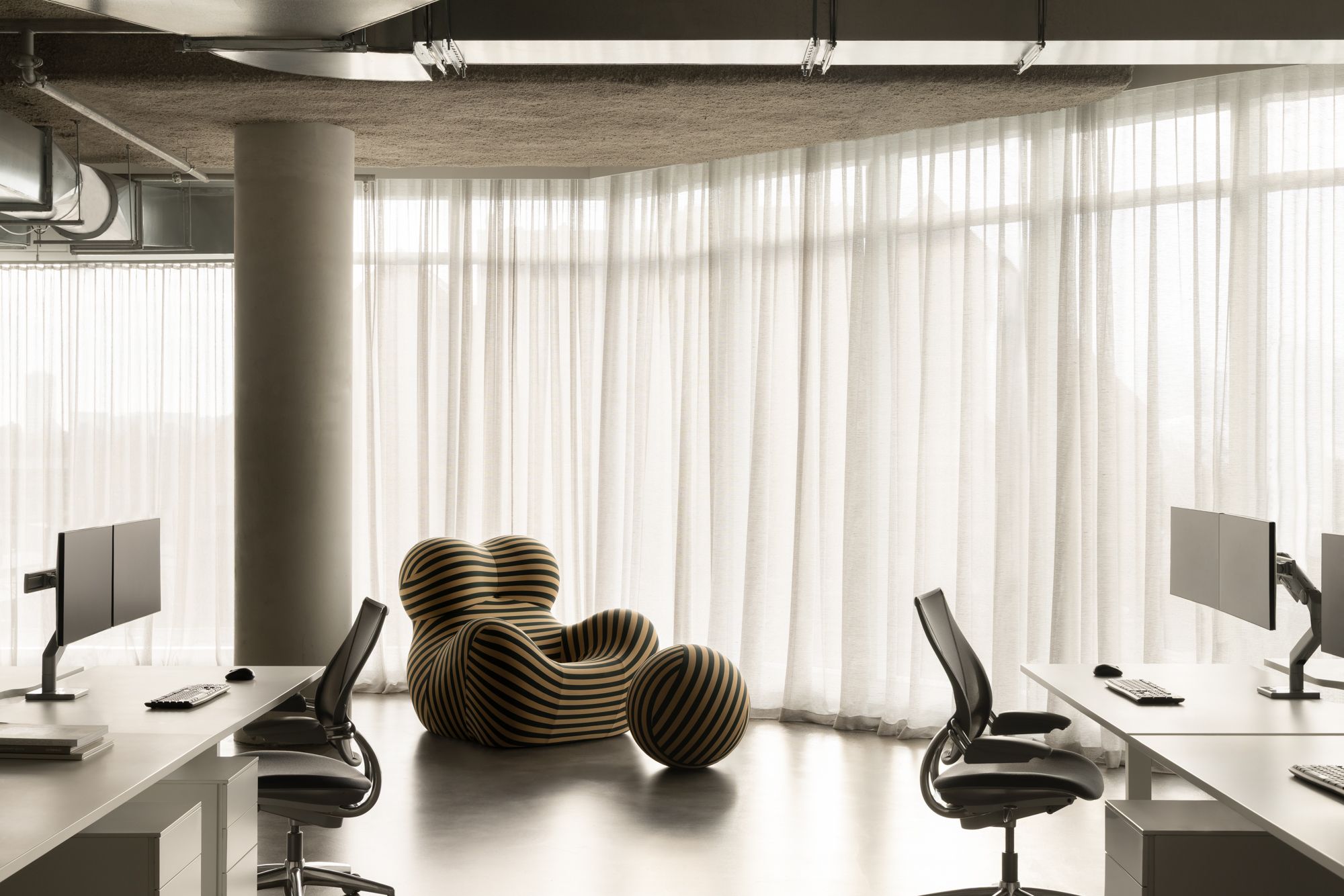 Studio McCue office interior with workstations, sheer curtains and striped B&B Italia Big Mama armchair.