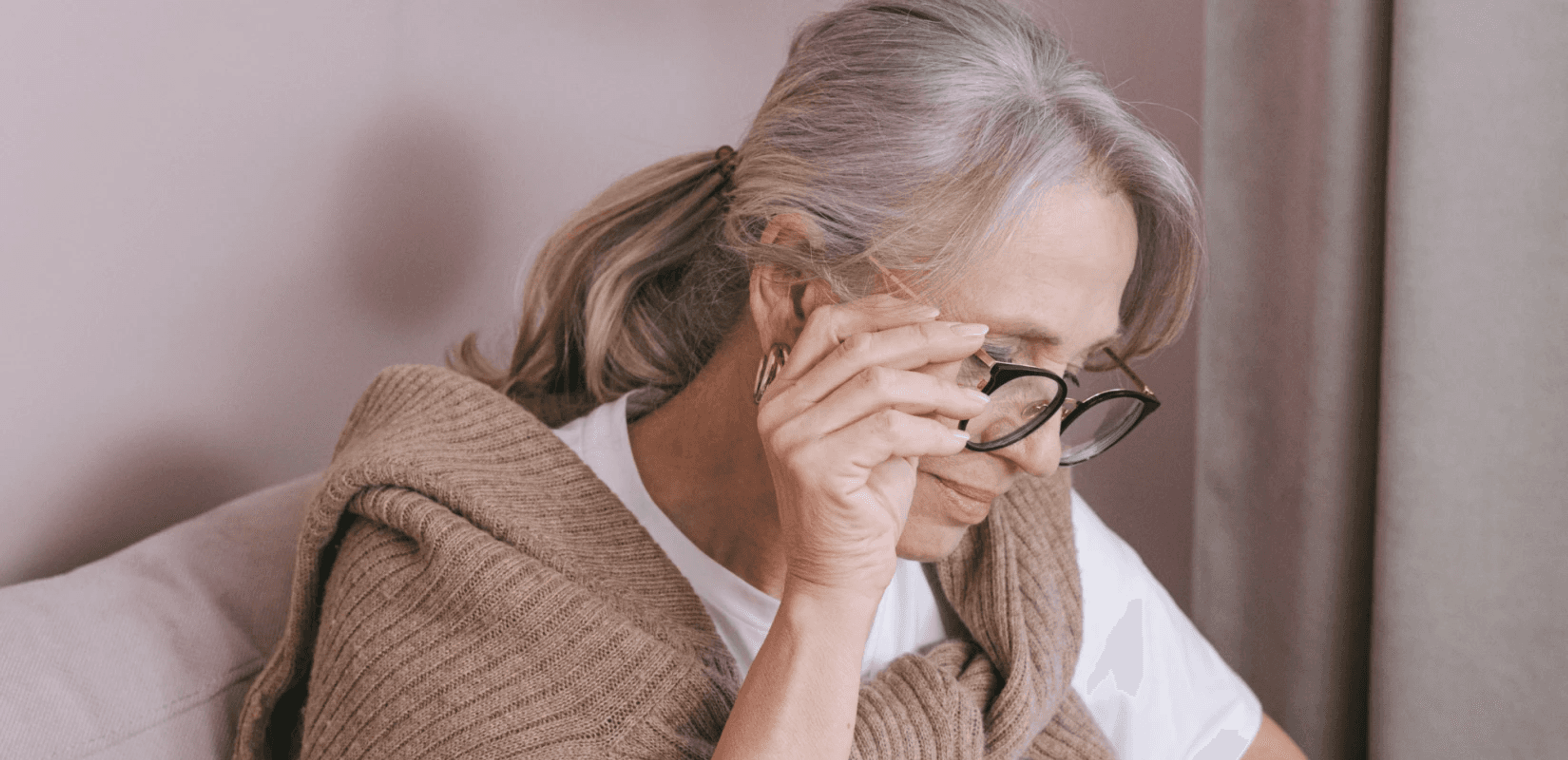 Ηλικιωμένη γυναίκα με γυαλιά κρατά σκεπτική το μέτωπό της, ανησυχώντας για τη σύνταξη χηρείας