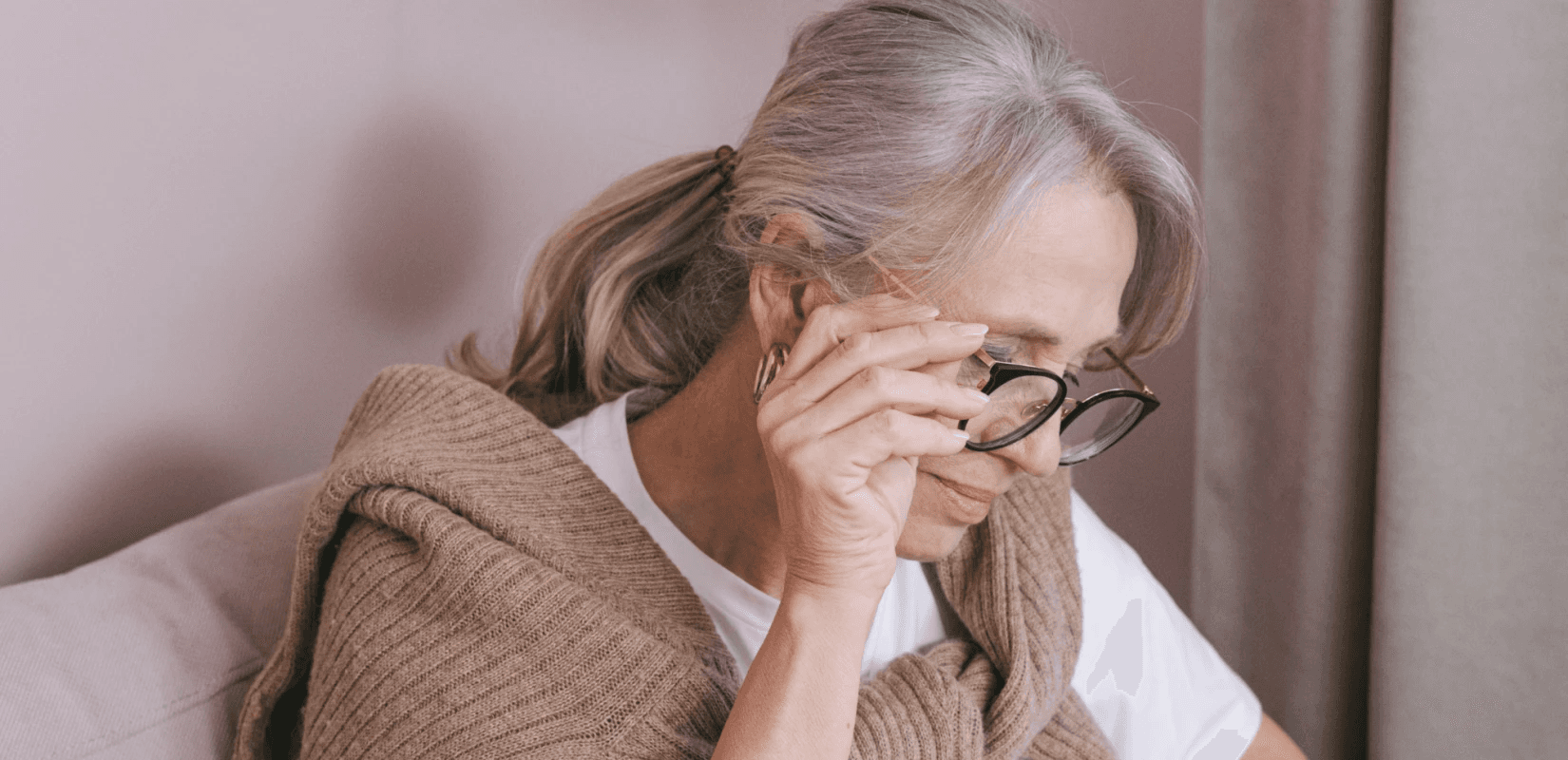 Ηλικιωμένη γυναίκα με γυαλιά κρατά σκεπτική το μέτωπό της, ανησυχώντας για τη σύνταξη χηρείας