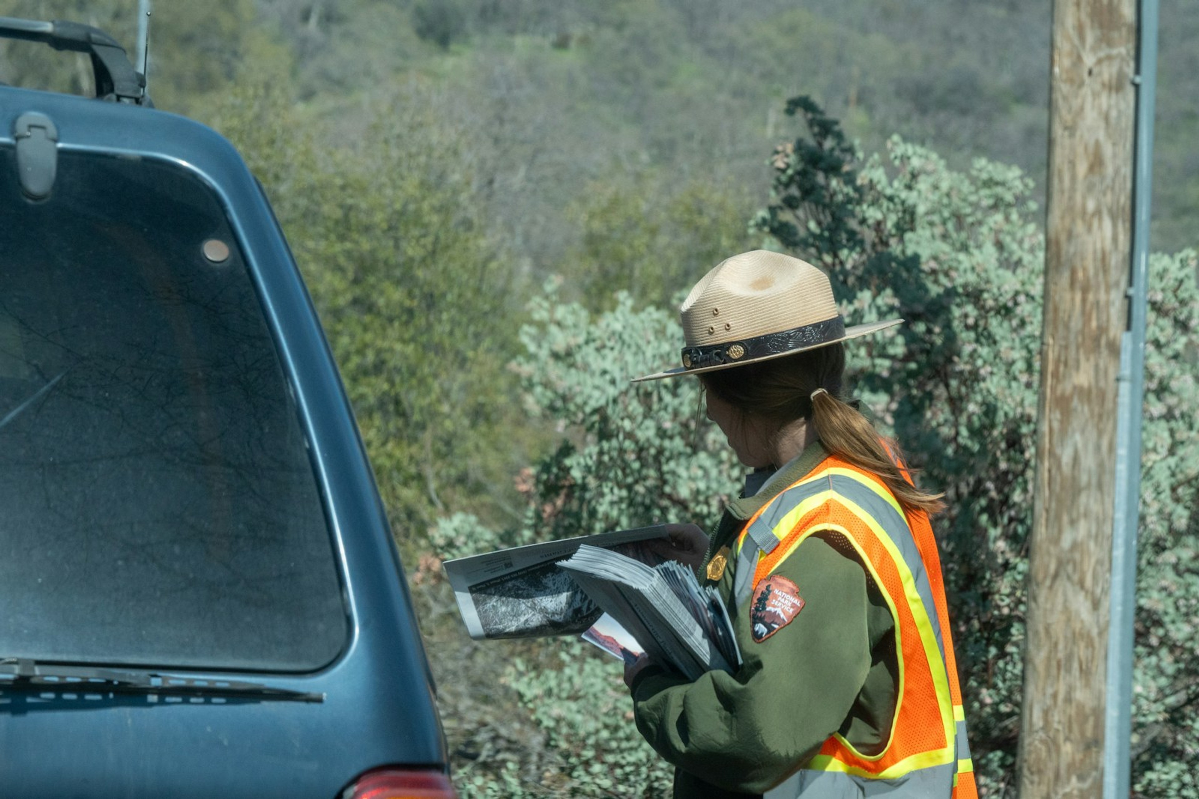 Person in high-visibility clothing with a laptop at a vehicle in the field