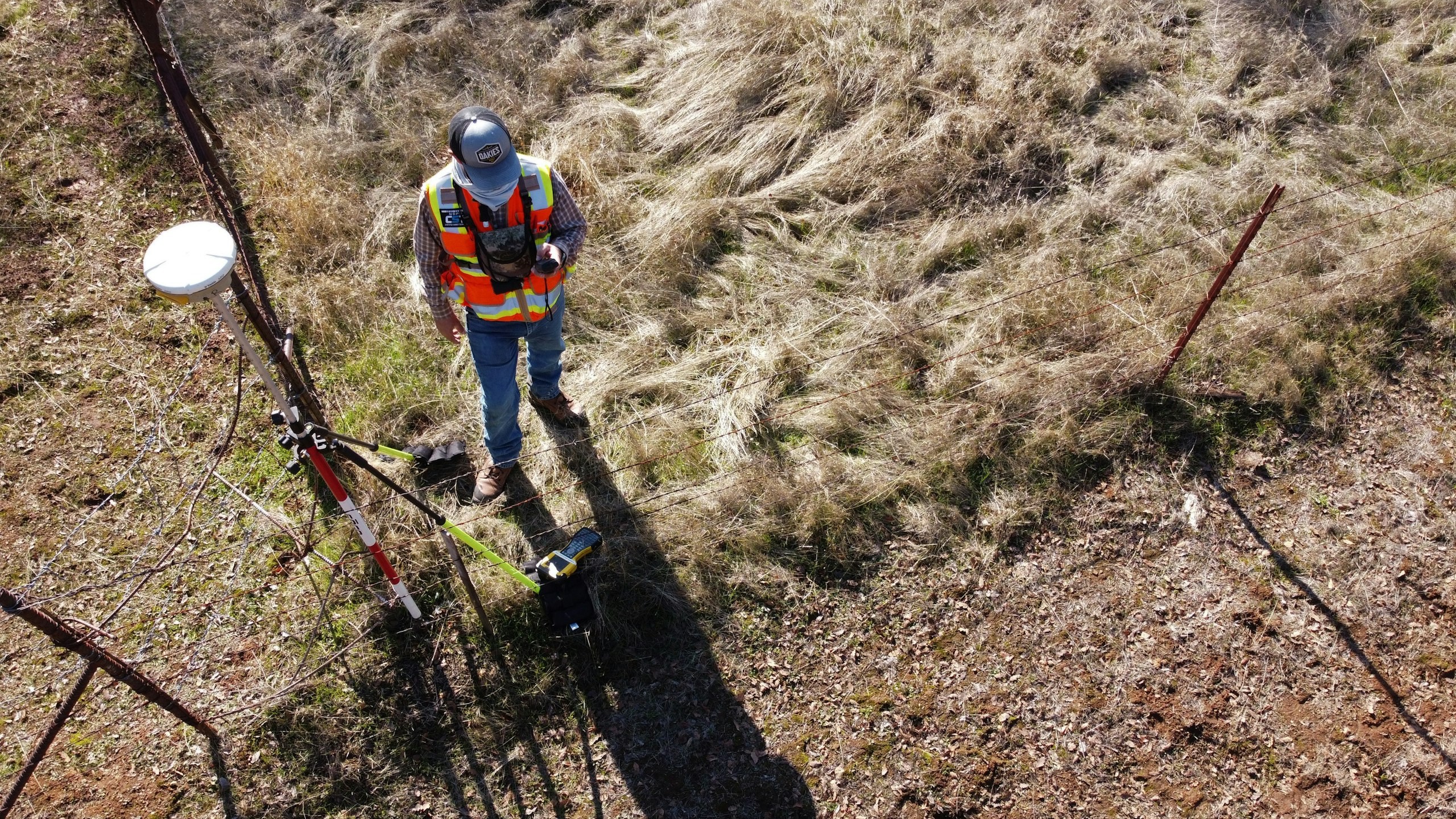 Surveyor with a GNSS antenna on dry terrain, captured from the air