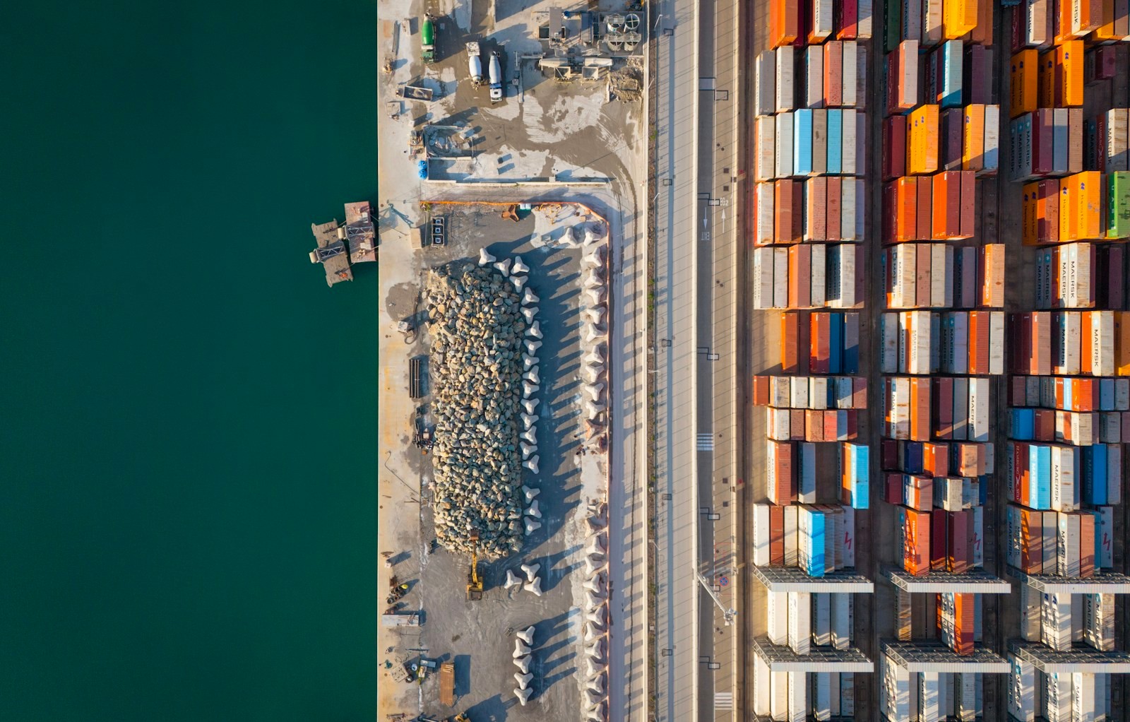 Shipping containers stacked in colour-sorted rows at a port terminal, seen from above