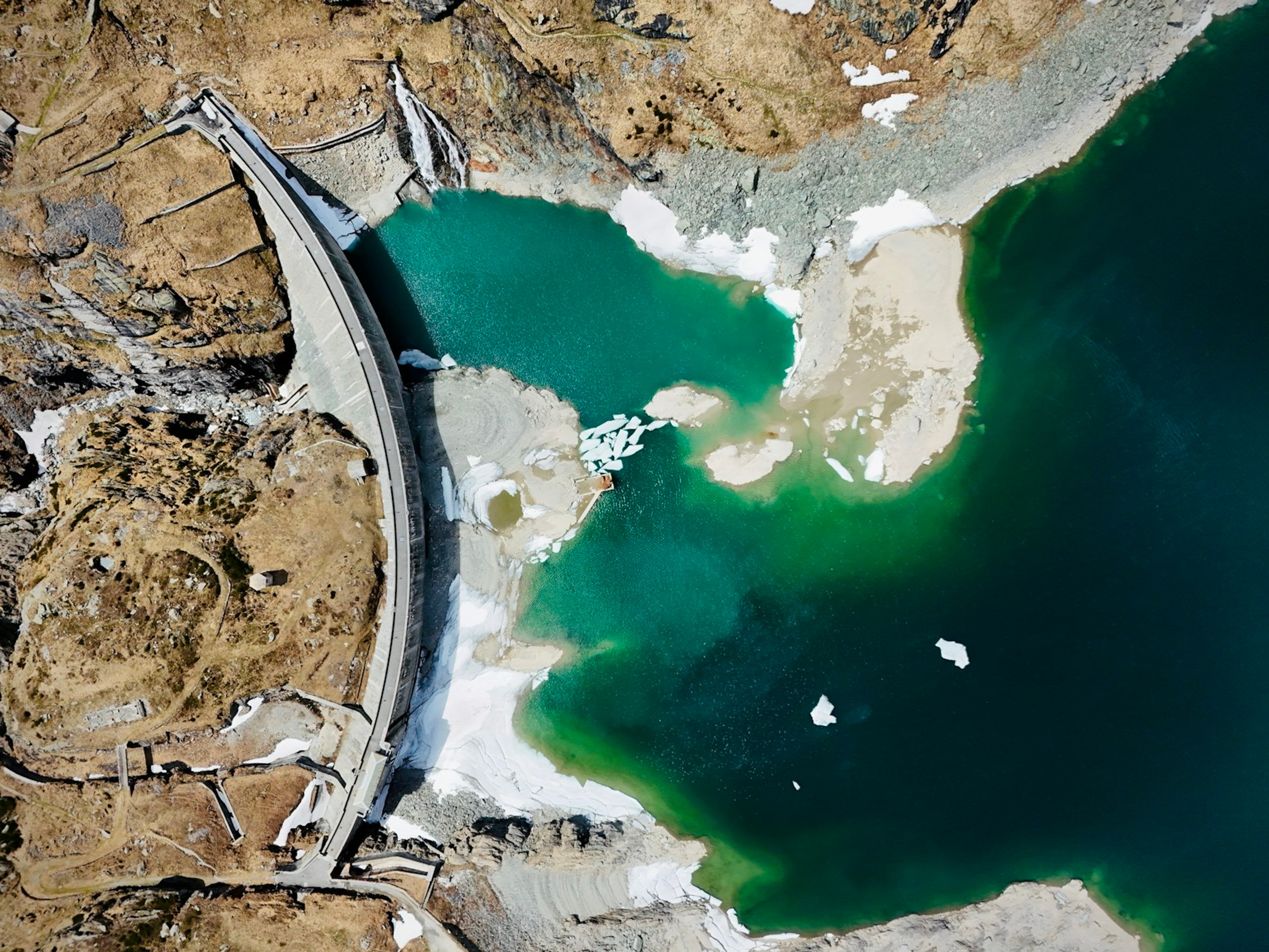 Dam wall with a turquoise reservoir, seen from directly above