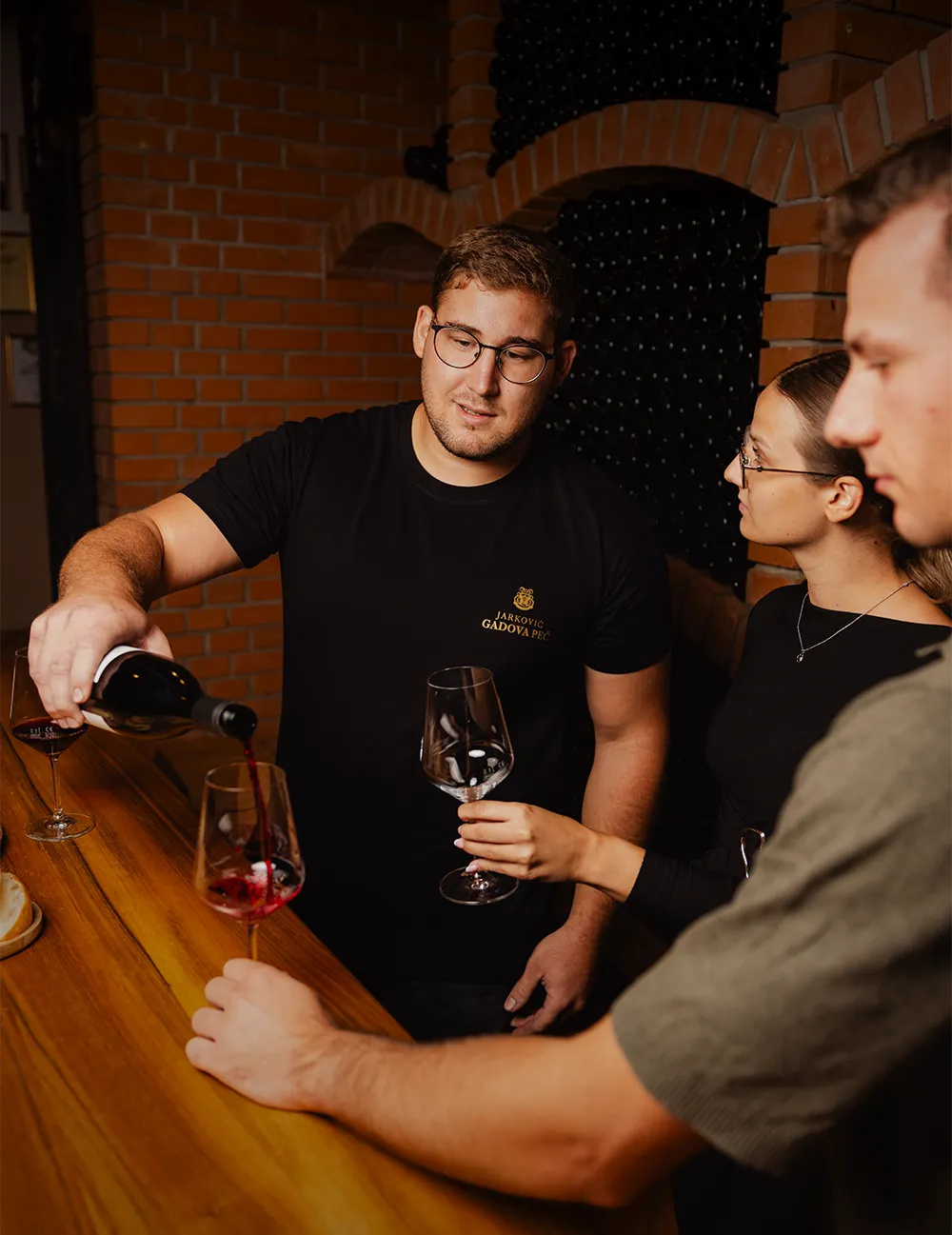 Jarkovič winemaker pouring red wine for guests at a wooden bar in the brick cellar