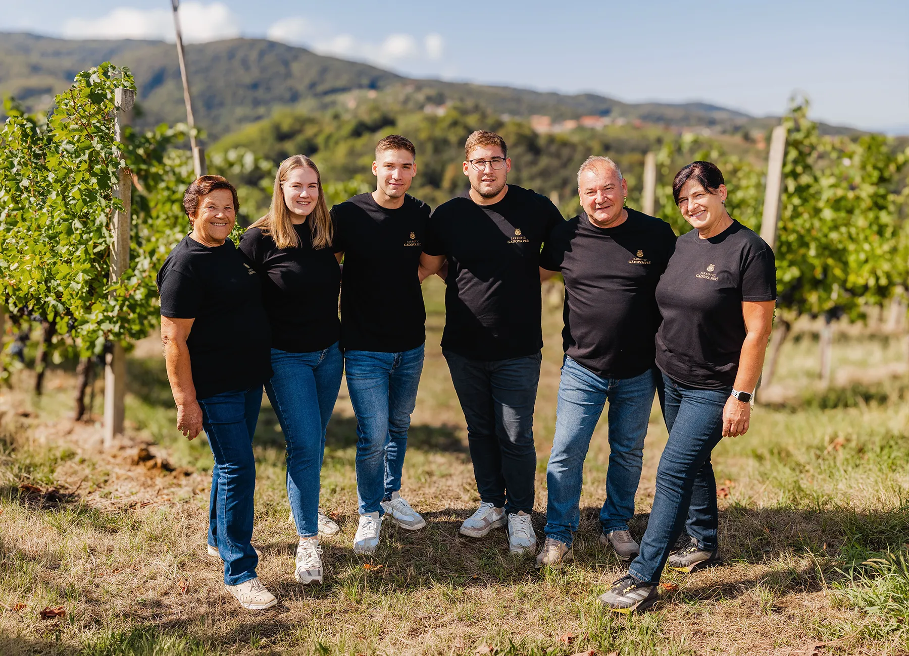 Six members of the Jarkovič family in black T-shirts standing in the vineyard with hills behind them