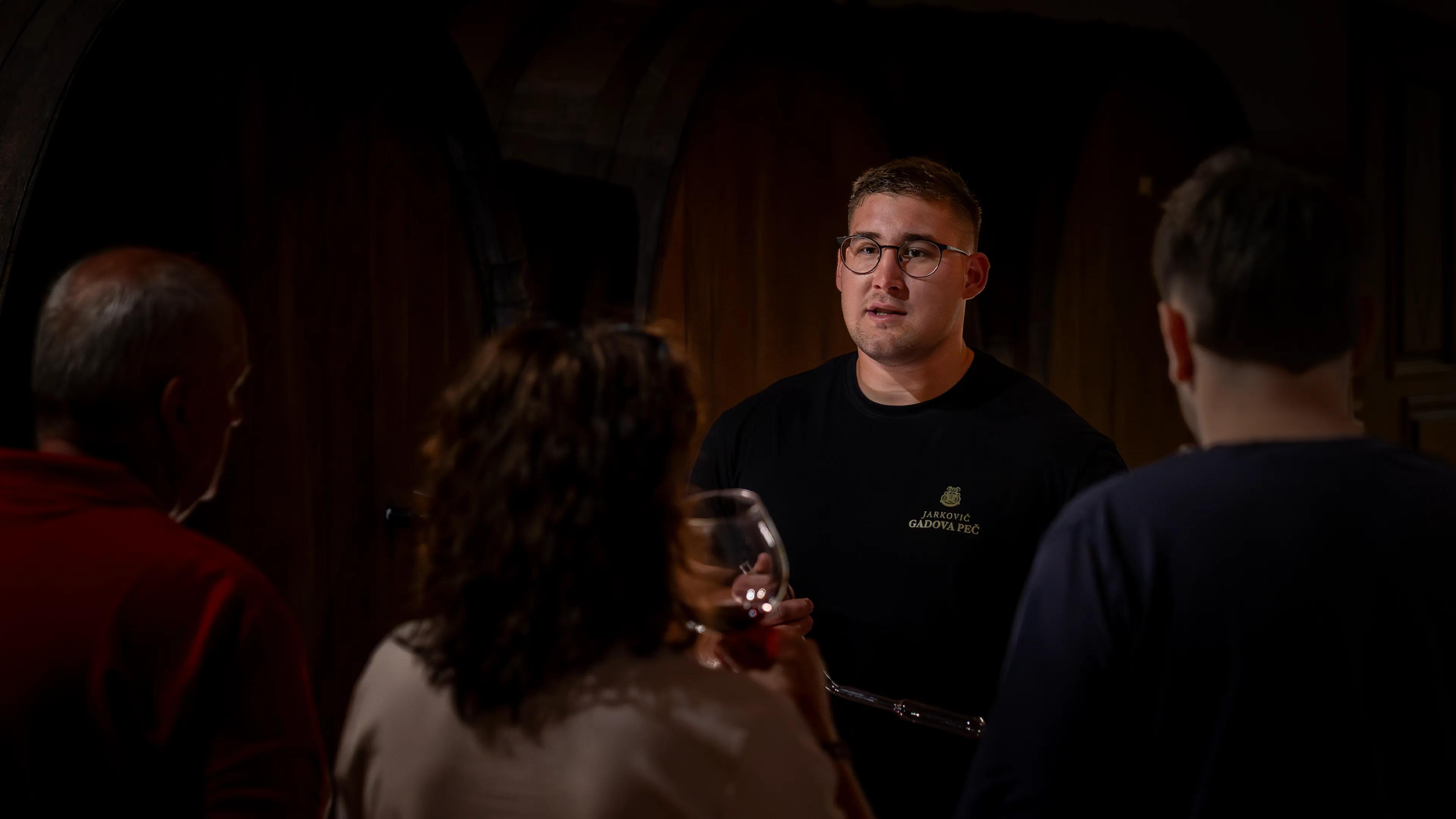 Young Jarkovič winemaker telling guests about the wines during a tasting in the dimly lit cellar