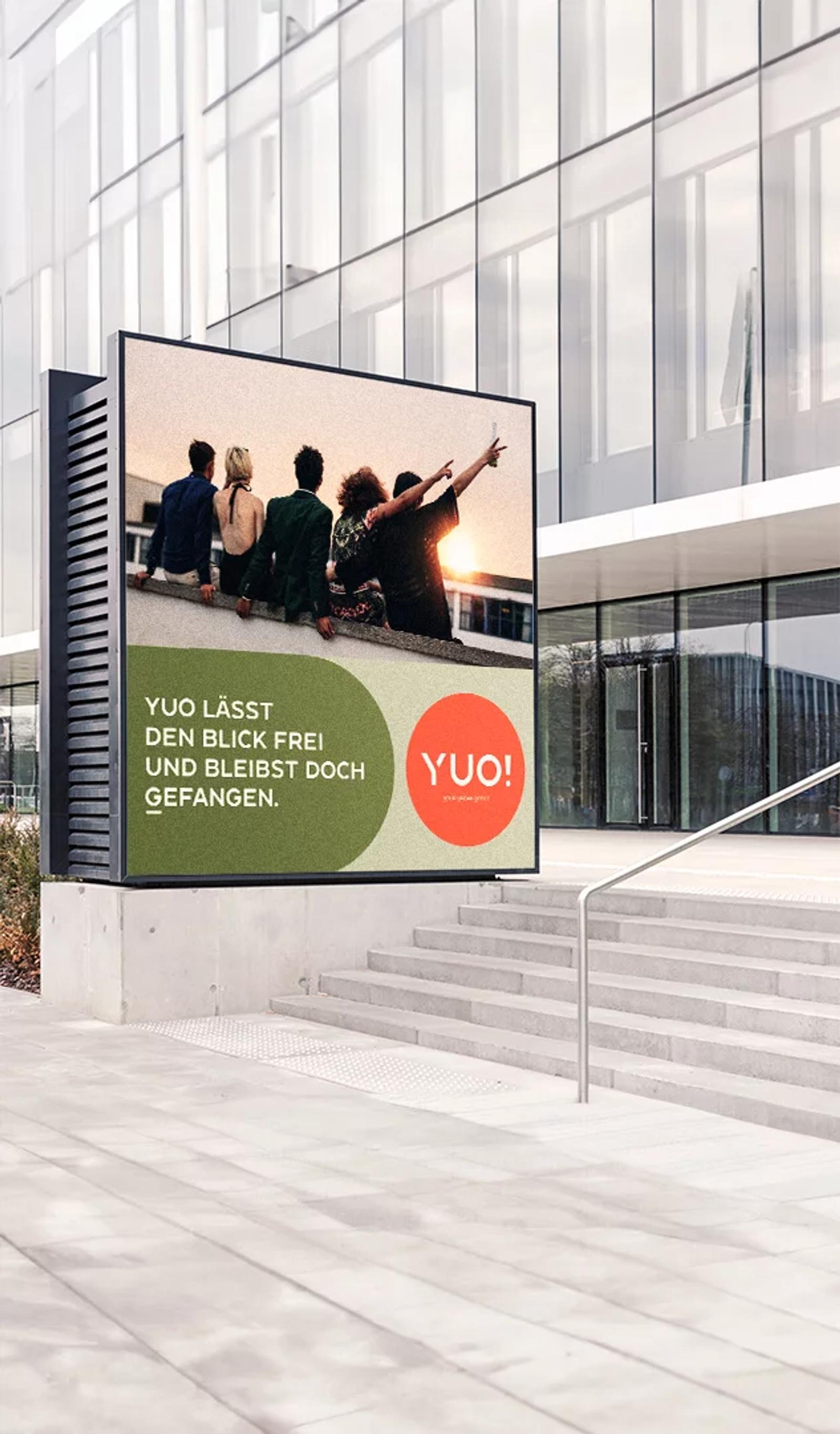 Freestanding city screen with the YUO! campaign line “YUO lässt den Blick frei und bleibst doch gefangen.”