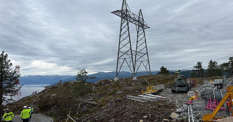 Kraftmast og anleggsutstyr i fjellterreng, med Sognefjorden og fjell i bakgrunnen.
