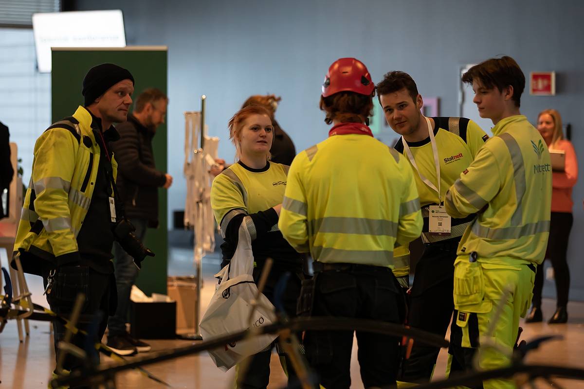 Energimontørlærlinger i arbeidsbekledning står i gurppe og snakker sammen underveis i finalen.