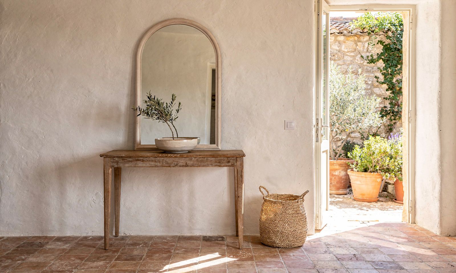 Entrance of a Provencal village house in Biot with an oak console, arched mirror and terracotta tomette floor