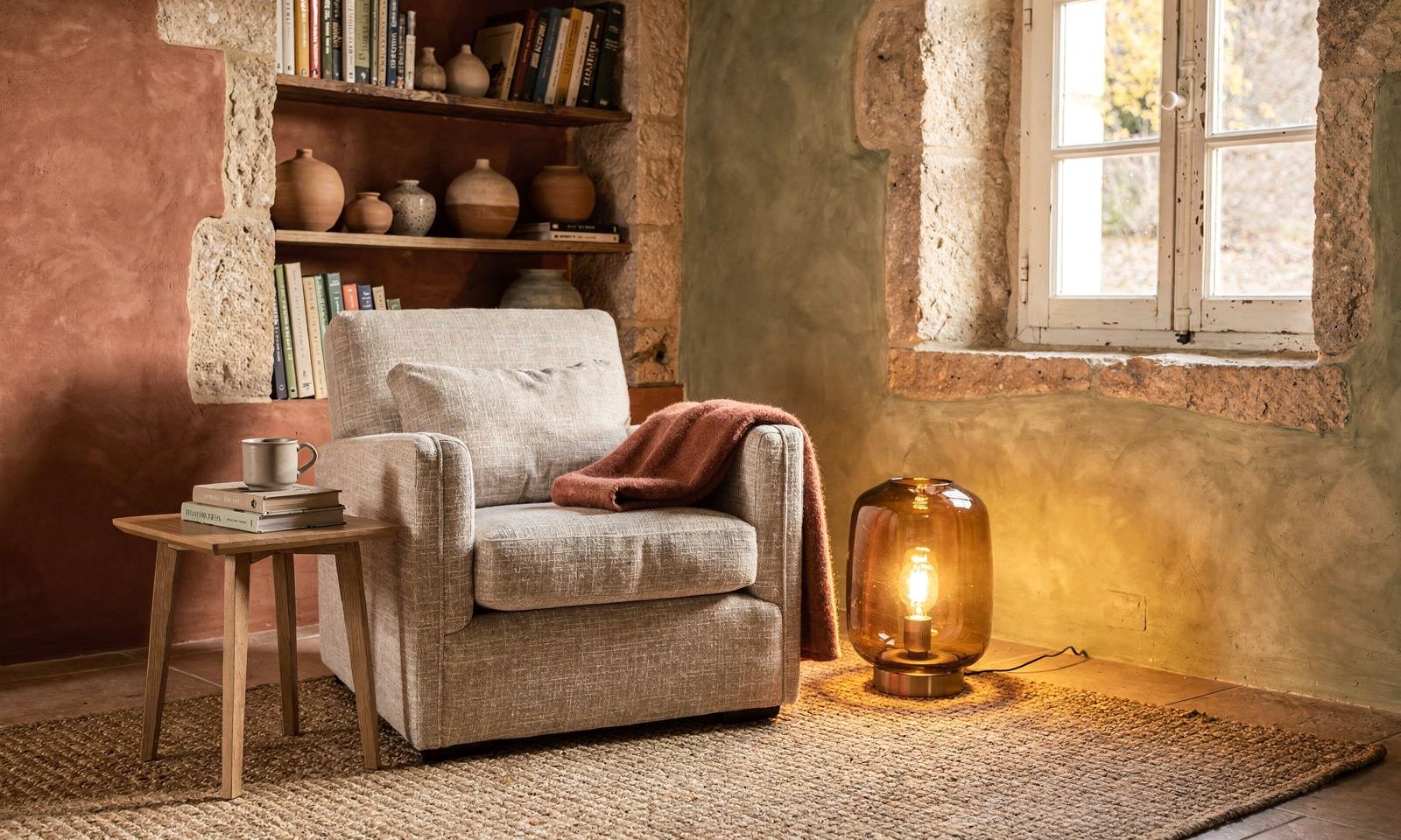 Coin lecture cosy avec fauteuil en lin, plaid et lampe en verre ambré dans une maison de village à Biot