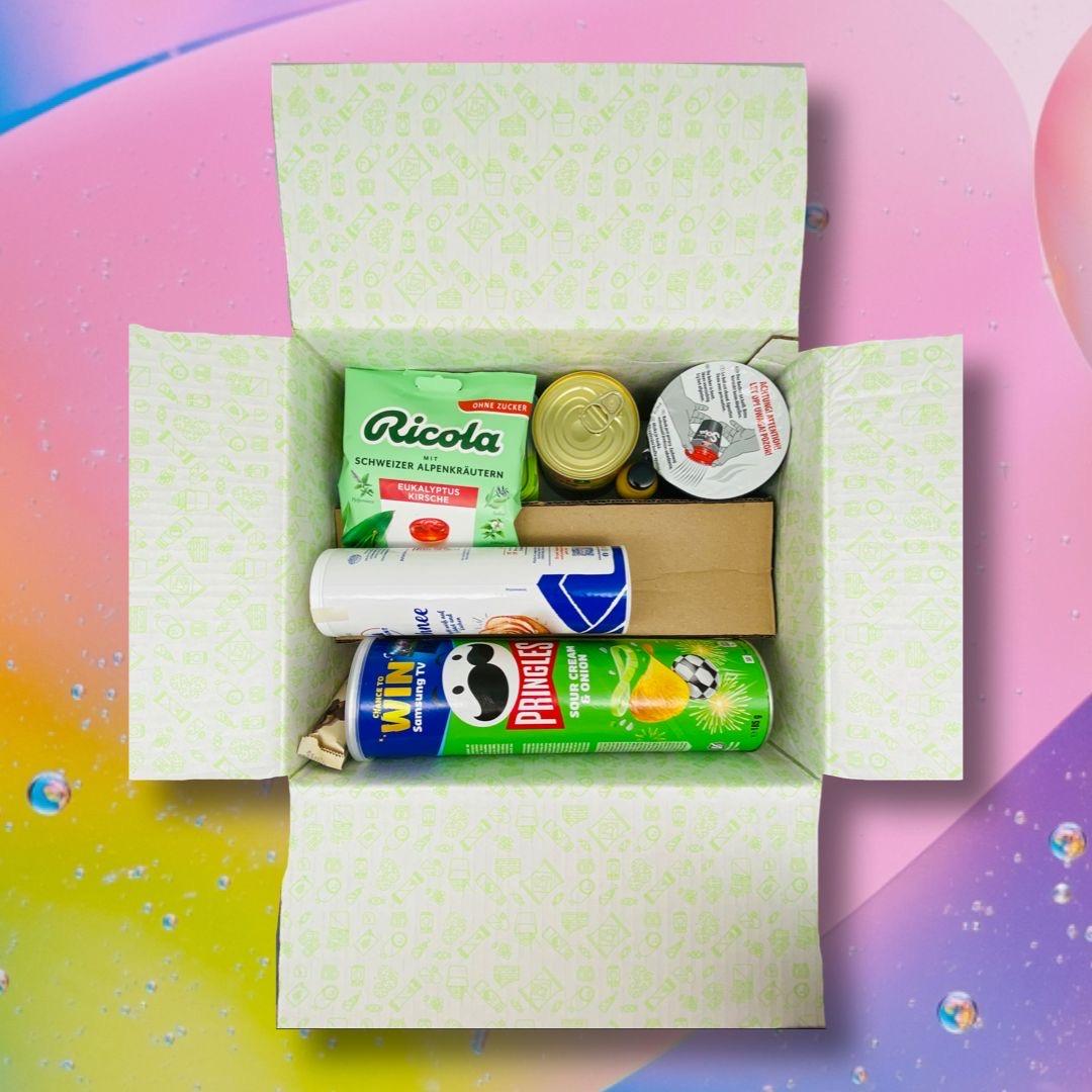 Degusta Box Karton mit verschiedenen Produkten gefüllt: Ricola, Pringels und weitere Lebensmittel.