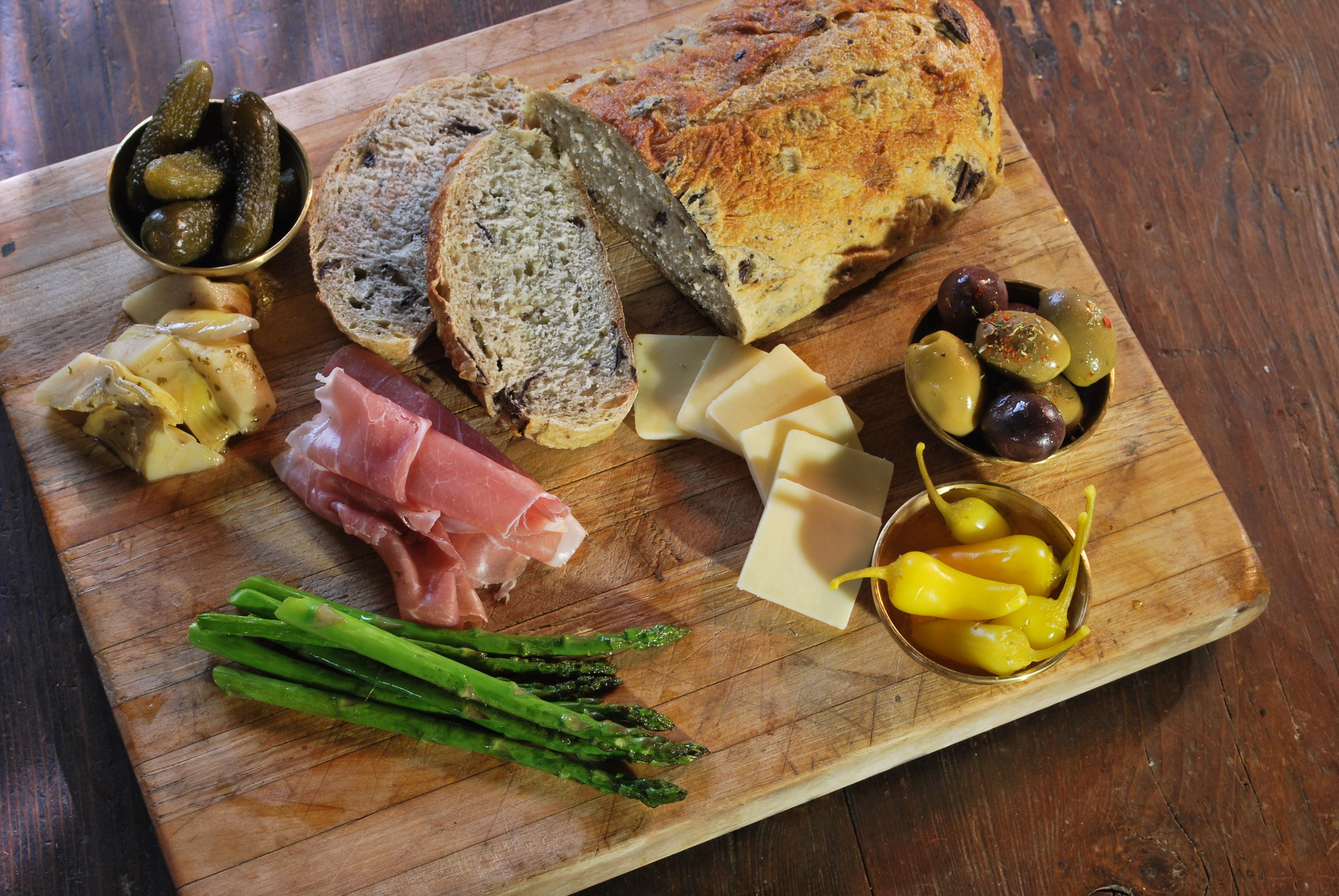 Oliven, Brot, Käse, Schinken, Sparkel, Gewürzugurken und Brot auf einem Holzbrett