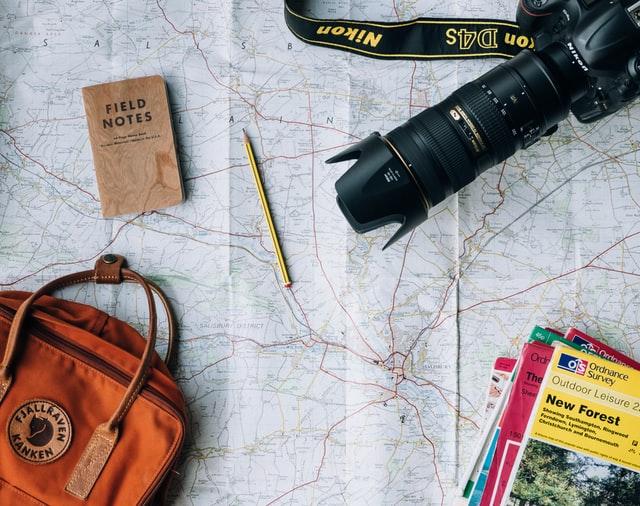 Eine Landkarte, auf welcher eine Kamera, ein Bleistift, in Notizblock und eine Tasche liegen.