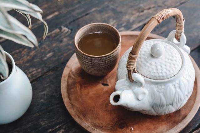 Eine weiße Teekanne und eine Teetasse auf einem Holztisch.