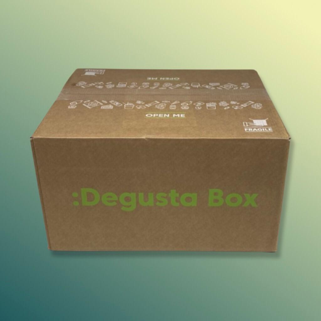 Degusta Box Karton mit bedrucktem Degusta Logo, ausgeschnitten vor einem grüngelbichen Hintergrund