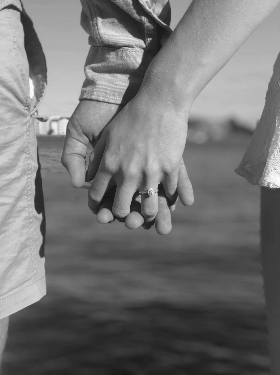 Two people recently engaged holding hands. The woman has an engagement ring on her hand.