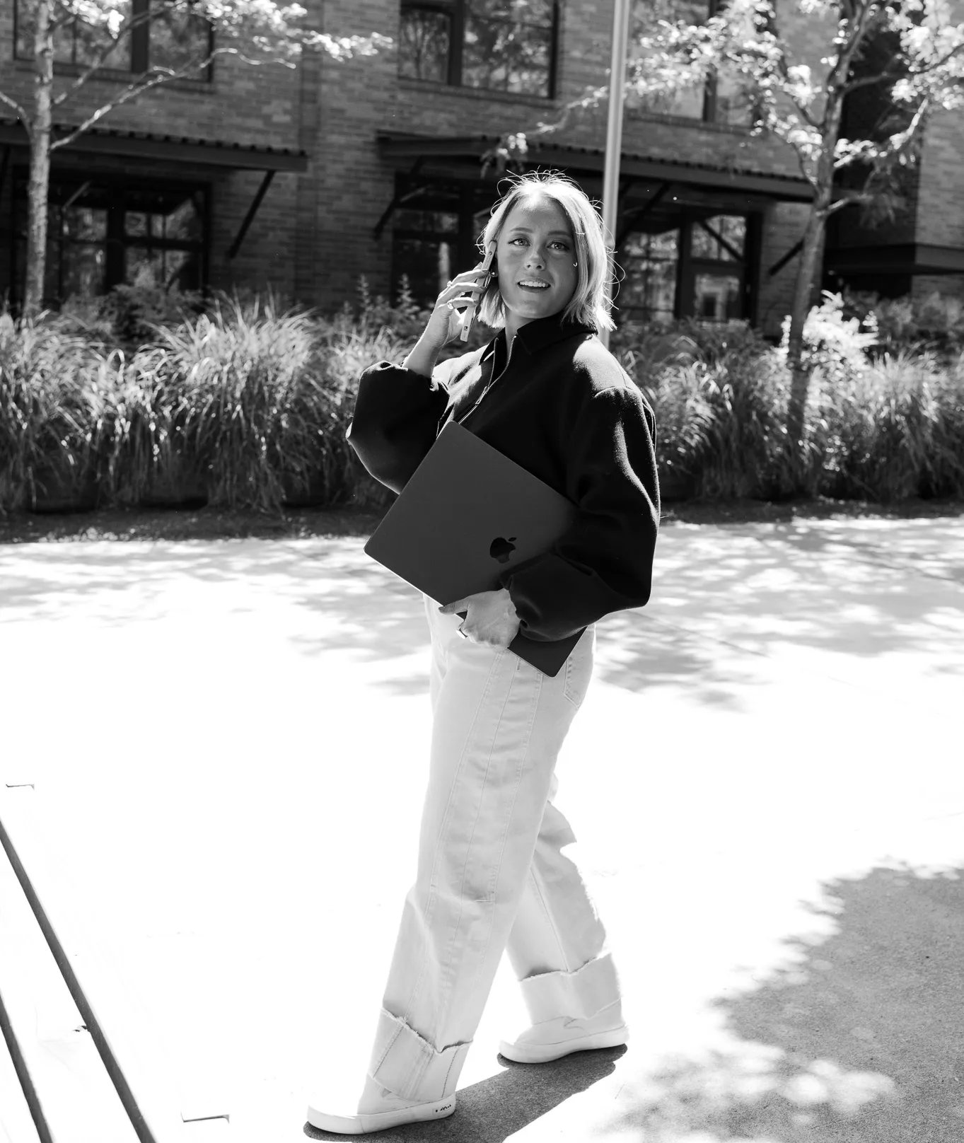 Black-and-white portrait of Olivia Krueger, Half + Half's branding and strategy co-founder, walking outdoors on a phone call while carrying a laptop.