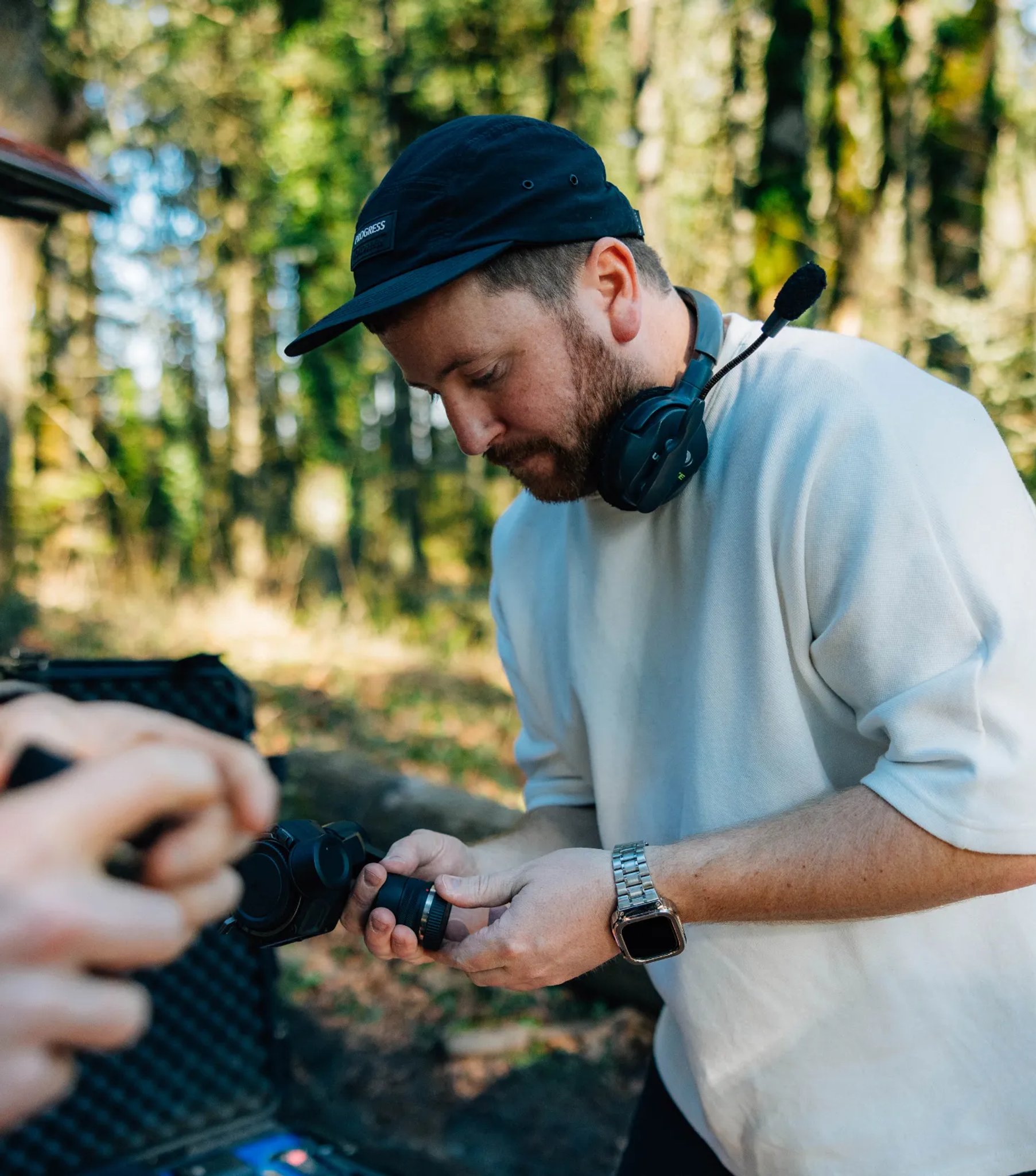 Man wearing a headset and cap changing a camera lens on a forest film set, illustrating the creative direction and photo/video service.