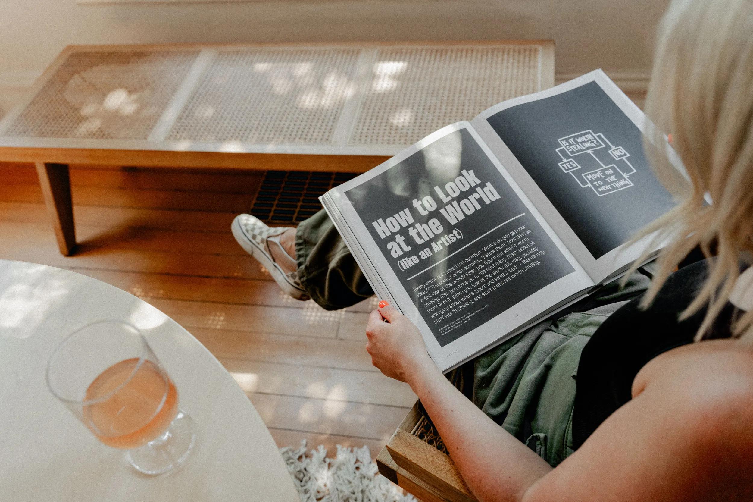 Overhead view of someone reading a spread titled 'How to Look at the World (Like an Artist)' beside a glass of rosé, illustrating the strategy and consultation service."