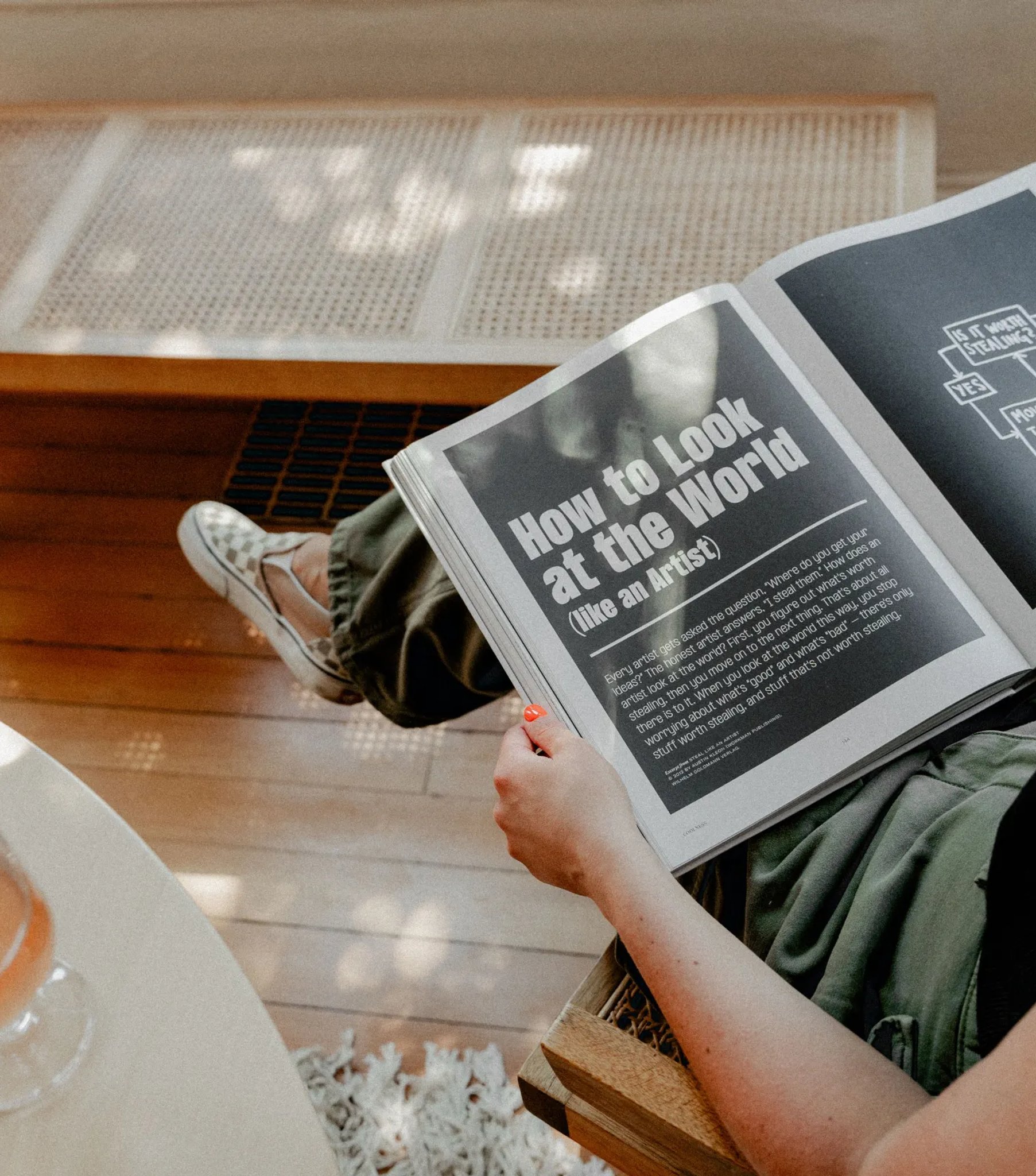 Overhead view of someone reading a spread titled 'How to Look at the World (Like an Artist)' beside a glass of rosé, illustrating the strategy and consultation service."