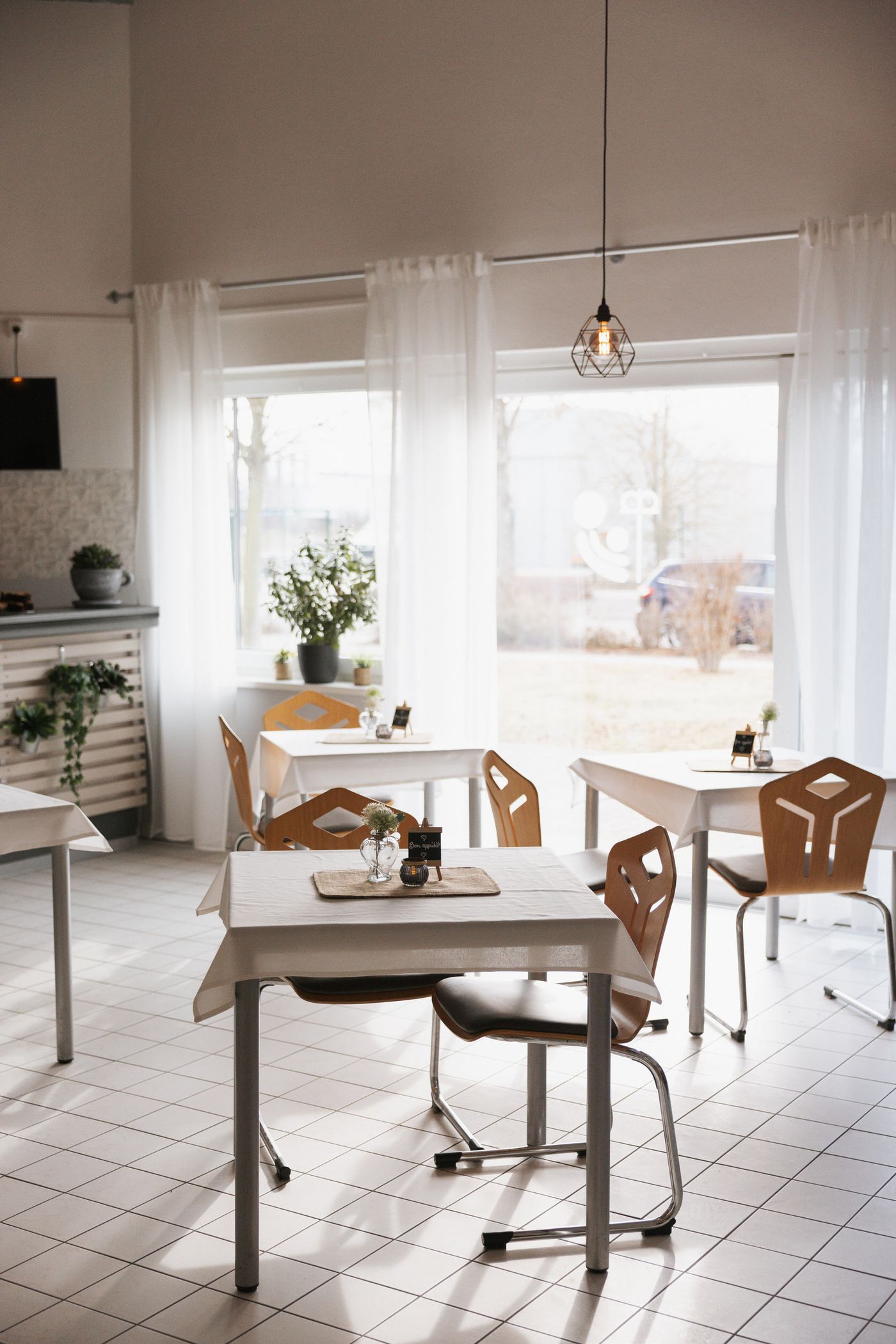Heller Gastraum des inklusiven Cafés mit Tischen am Fenster