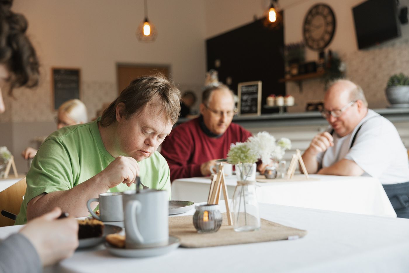 Beschäftigte und Gäste sitzen gemeinsam an einem Tisch im Café – ein Ort der Begegnung