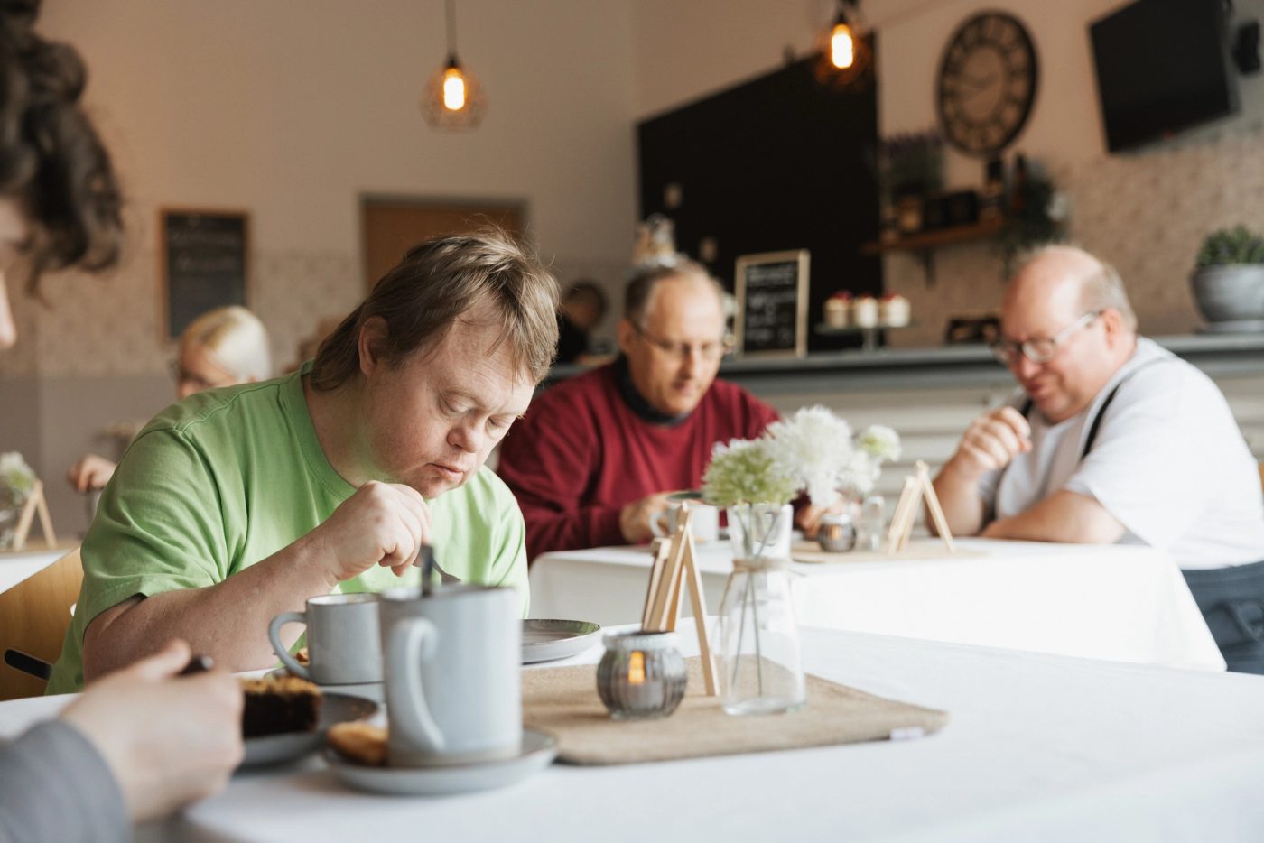 Beschäftigte und Gäste sitzen gemeinsam an einem Tisch im Café – ein Ort der Begegnung