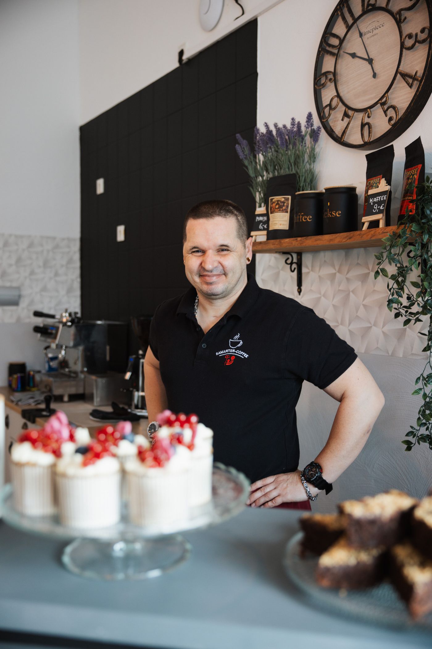 Barista des Cafés steht stolz hinter der Theke mit selbstgemachten Kuchen