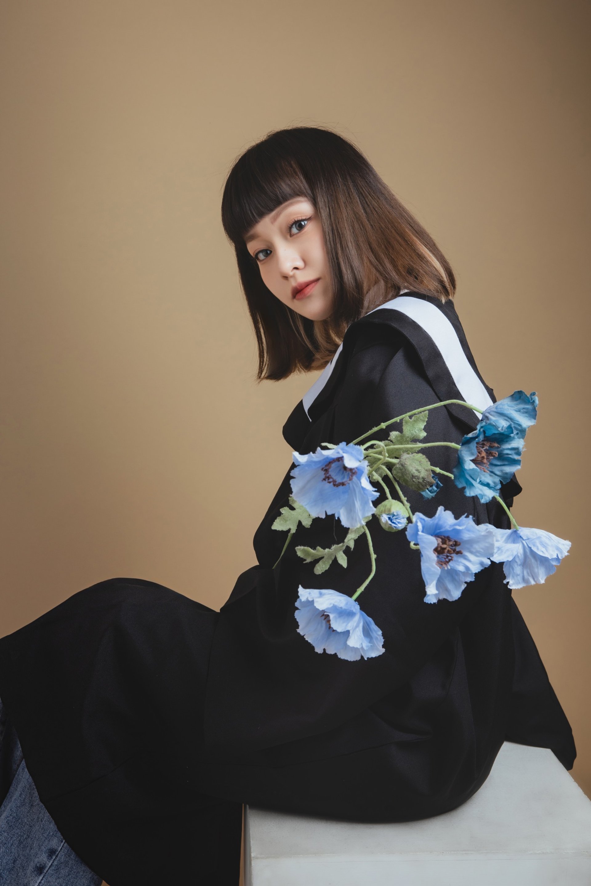 畢業寫真－黑色學士服女性手持藍色花束卡其色背景
