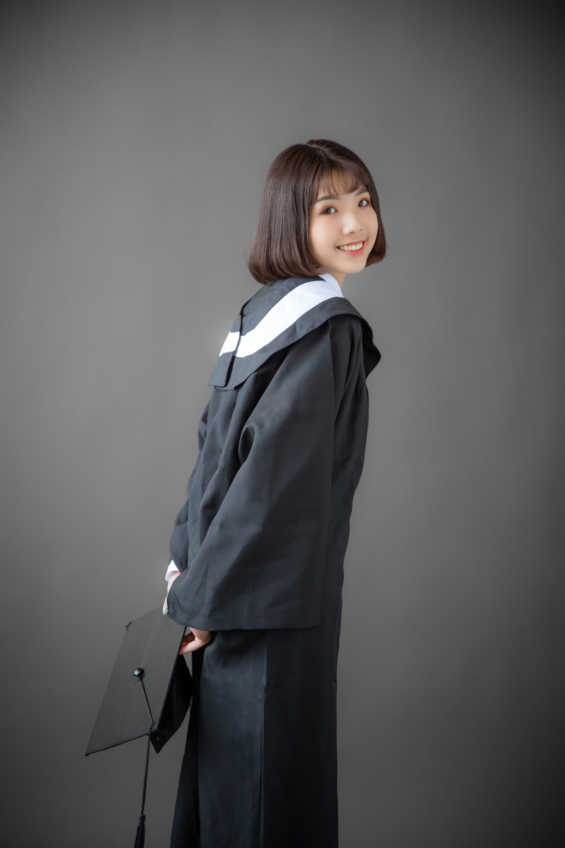 畢業寫真－短髮女性回眸手持學士帽深灰背景