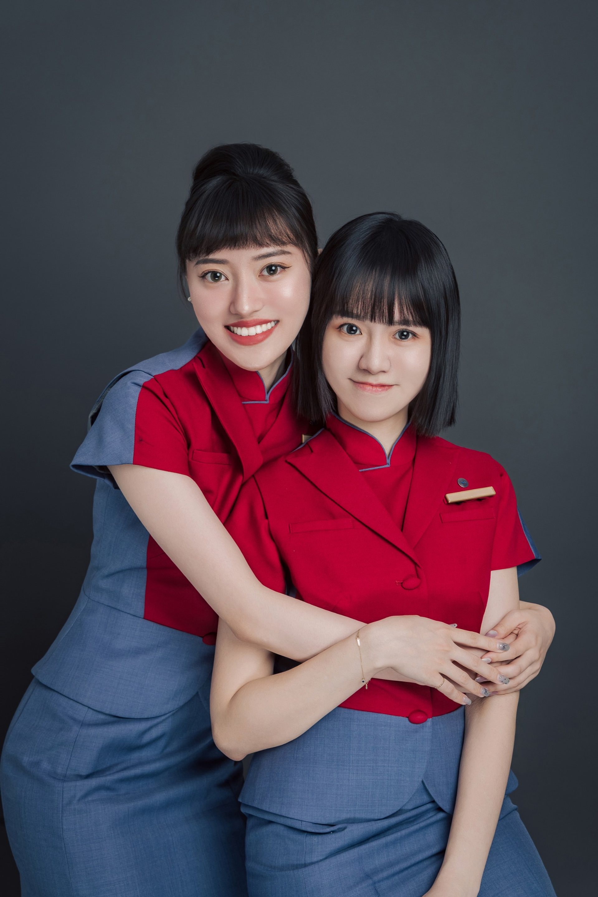 閨蜜寫真－兩位紅藍制服女性相擁微笑深灰背景