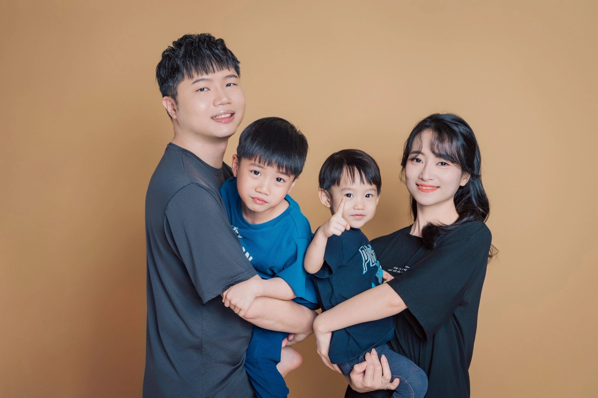 全家福寫真－四口之家深色上衣抱兩幼童棕色背景