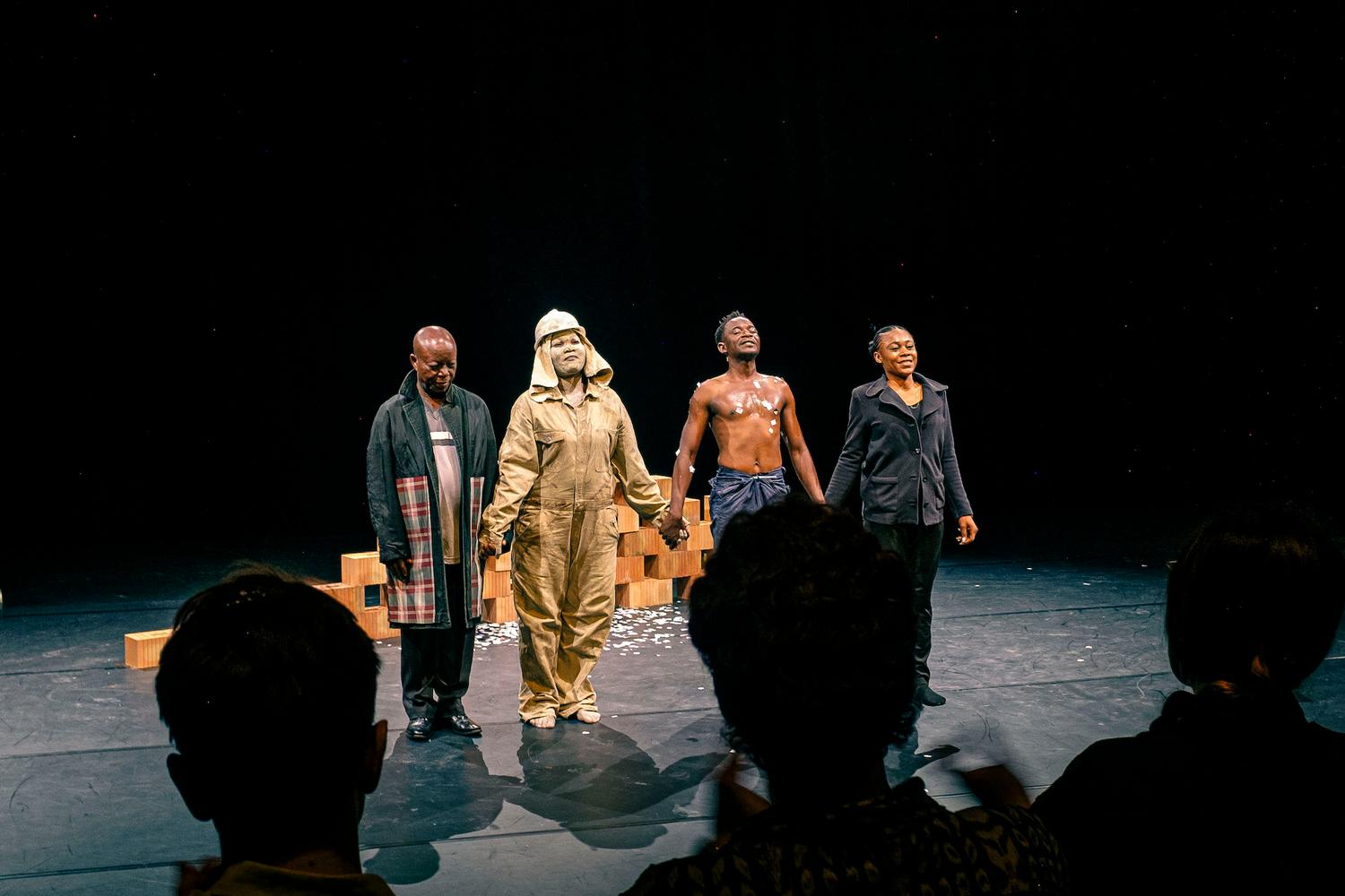 Das Bild zeigt vier Menschen auf einer Bühne. Sie lächeln und halten sich an den Händen.