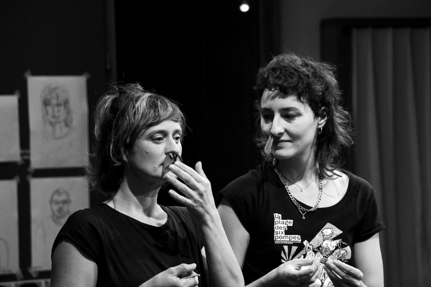 Eine Schwarz-Weiss-Fotografie zeigt die Oberkörper zweier weiblich gelesener Personen, in deren Nasenlöchern Salbei steckt.