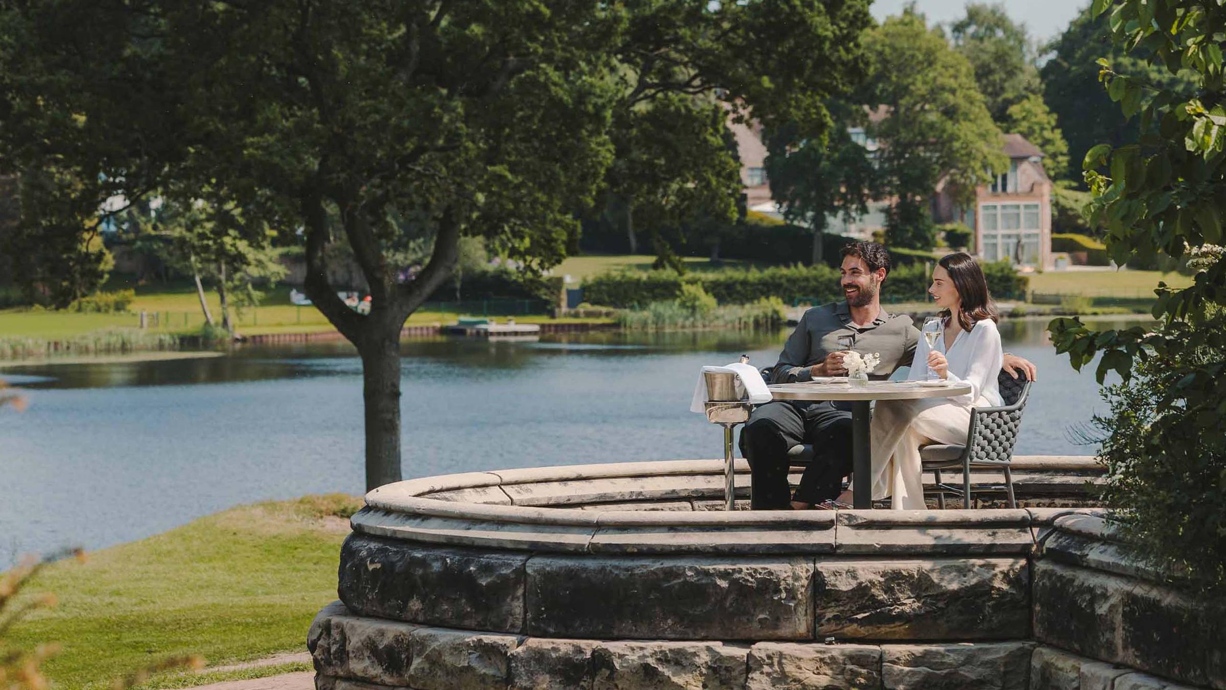 A couple sharing a toast at a lakeside table on the estate