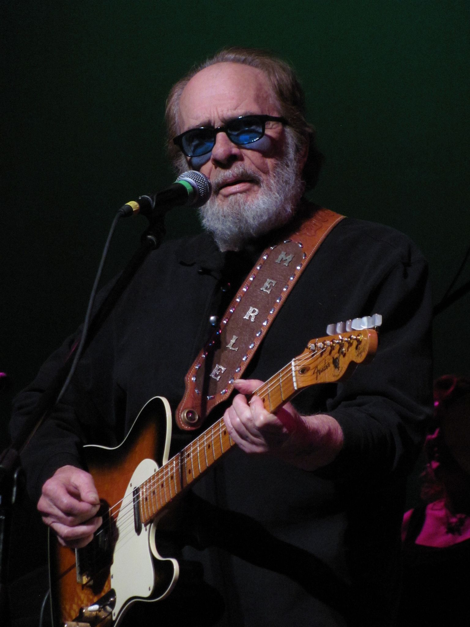 Merle Haggard singing and playing guitar on stage in concert