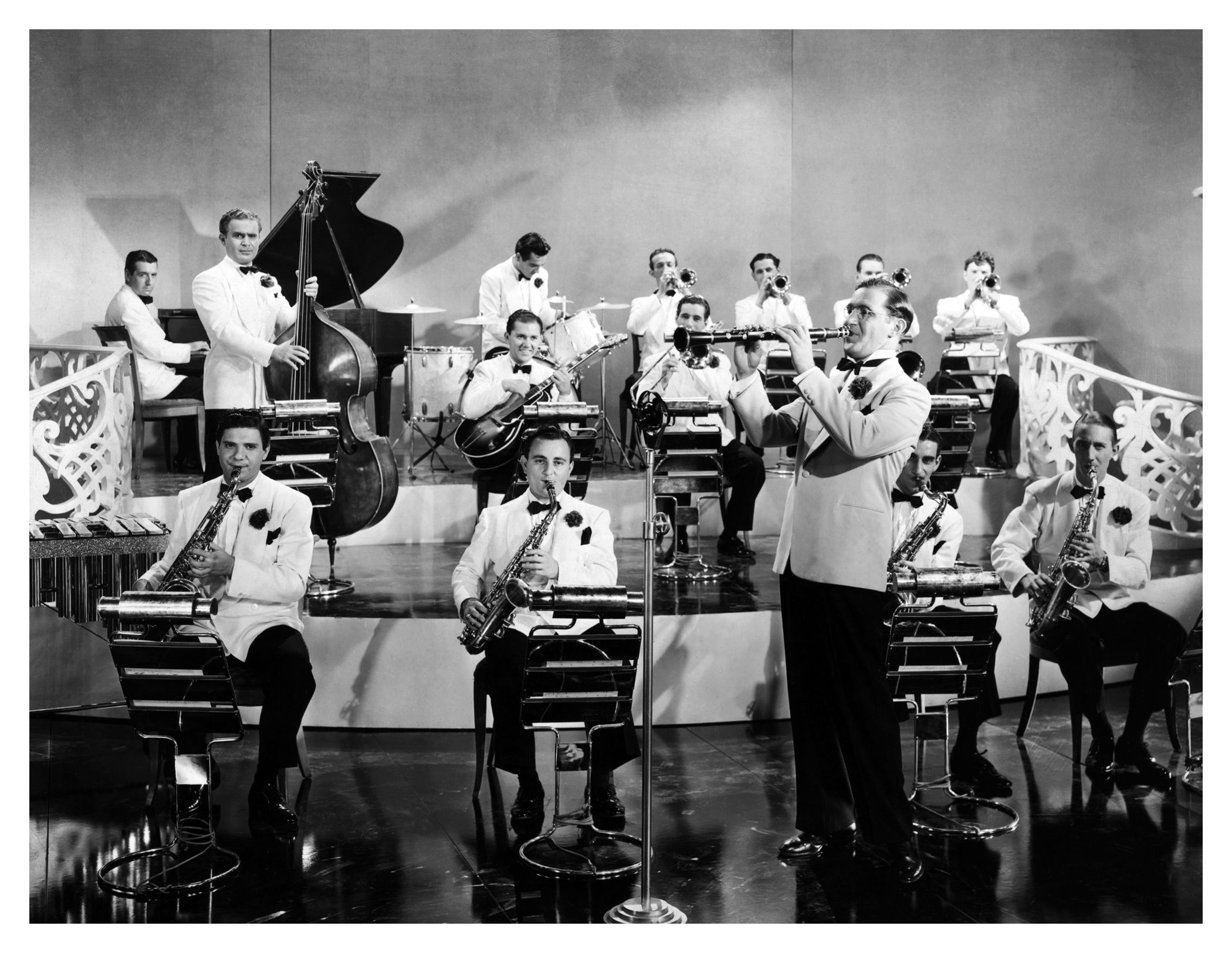 A black and white photo of a big band performing on a stage, with a clarinetist standing in the foreground.