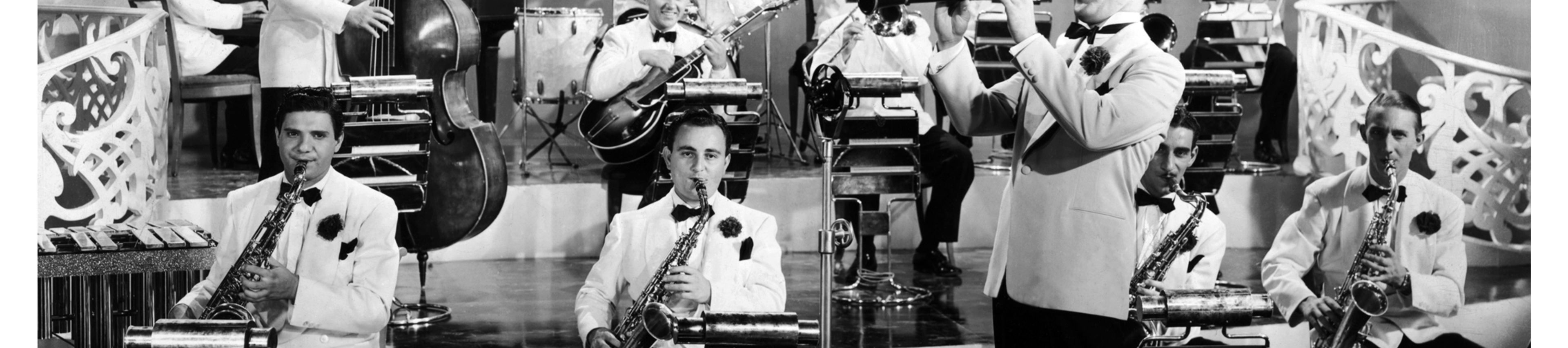 A black and white photo of a big band performing on a stage, with a clarinetist standing in the foreground.