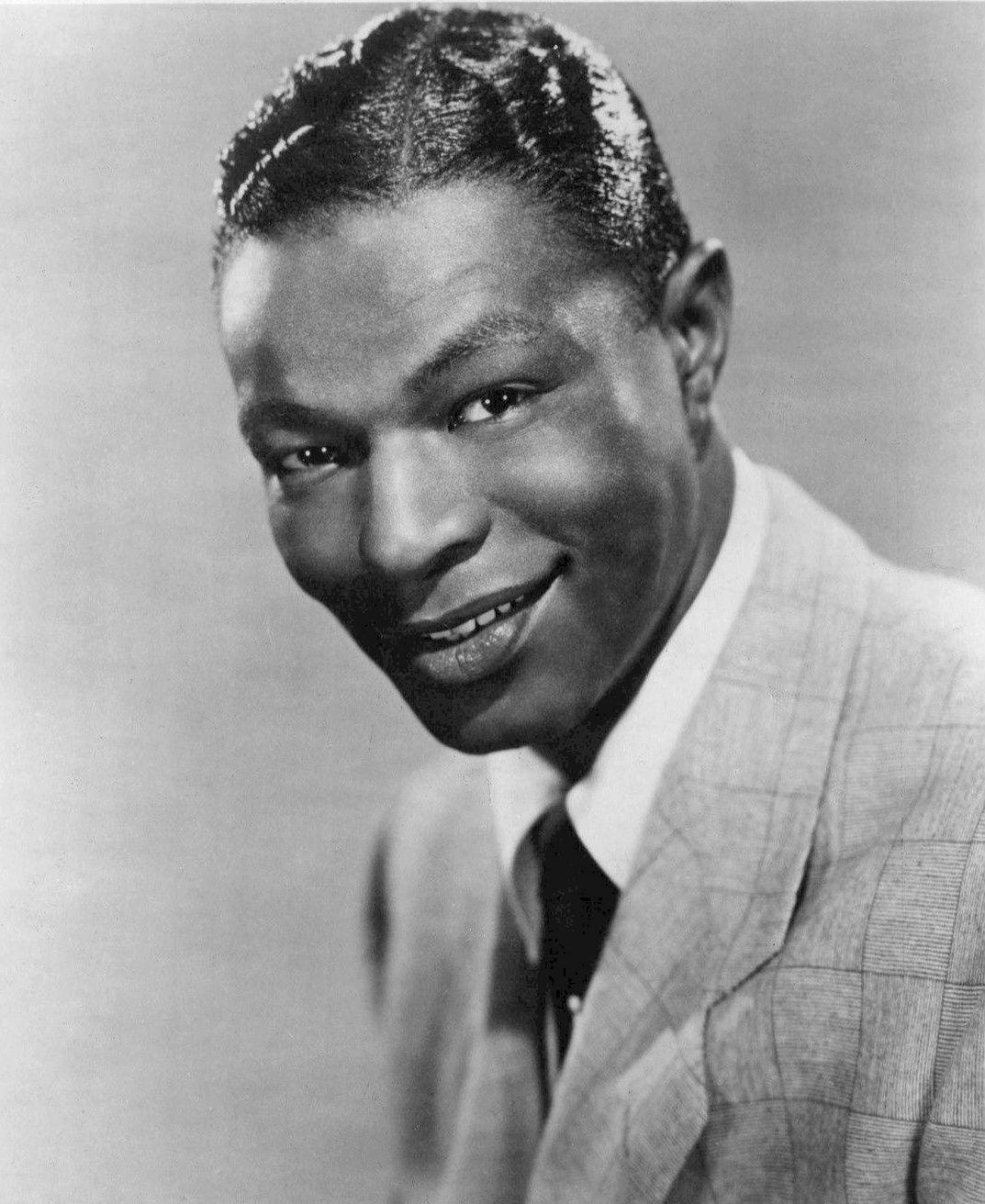 Black-and-white publicity portrait of Nat King Cole in a suit, smiling.